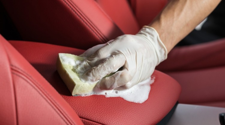 man carefully scrubbing his red leather car seat