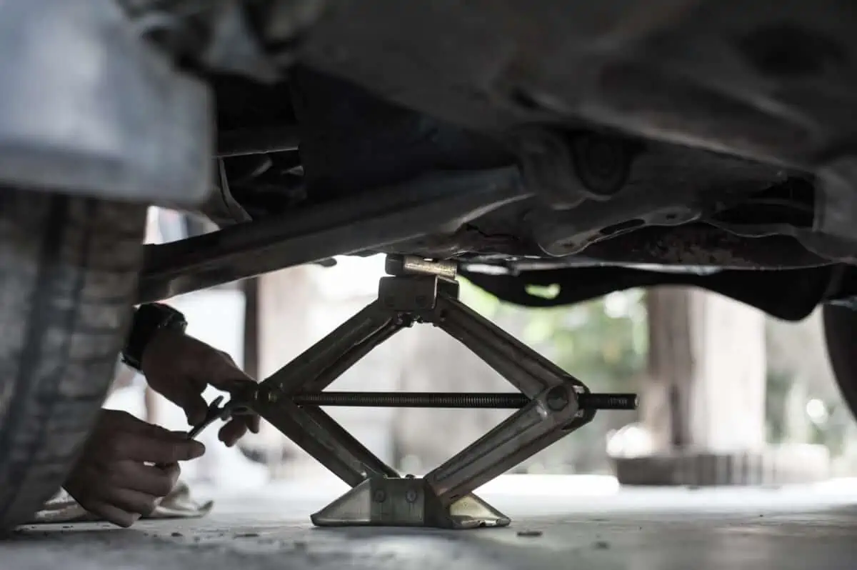 A black scissor jack underneath and holding up a car