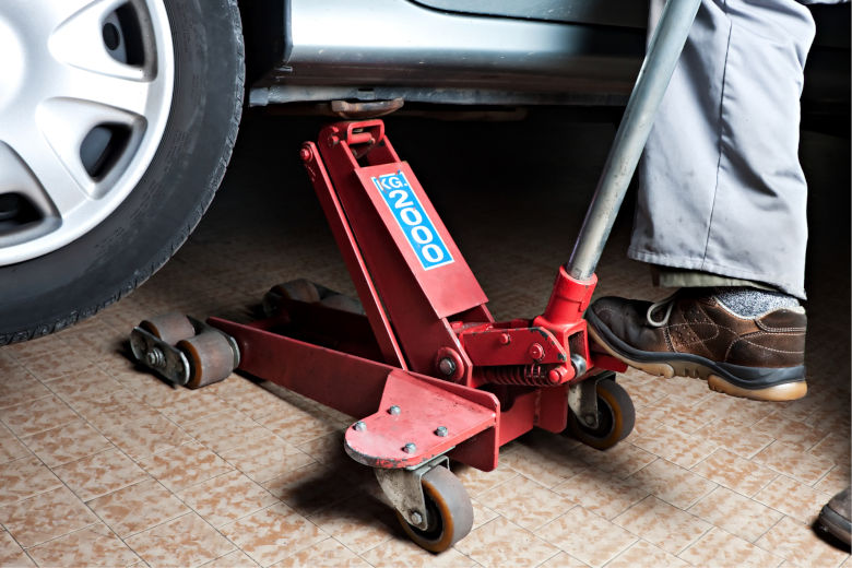 A red floor jack lifting a silver car during a tire change