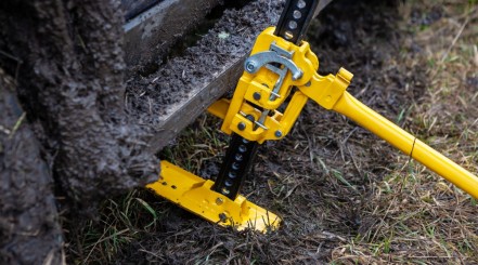 A yellow high lift jack being used to lift a 4x4 that's stuck in some deep mud