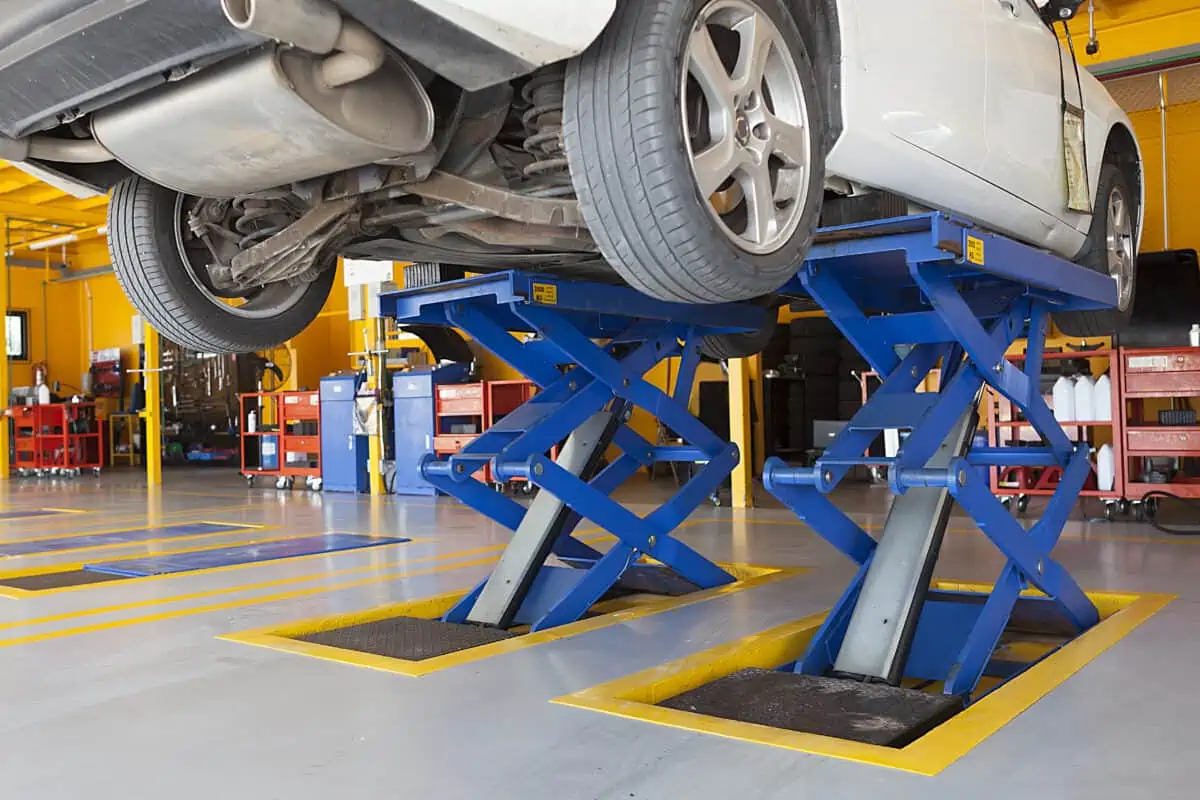 Large, blue hydraulic scissor jacks holding up a white car in a a garage