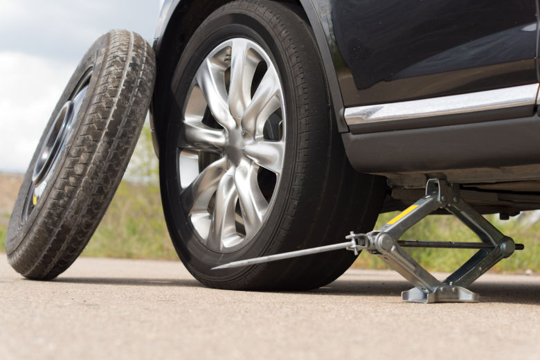 Grey scissor jack lifting up a black car for a tire change