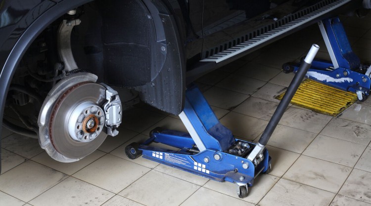 A blue floor jack under a car having it