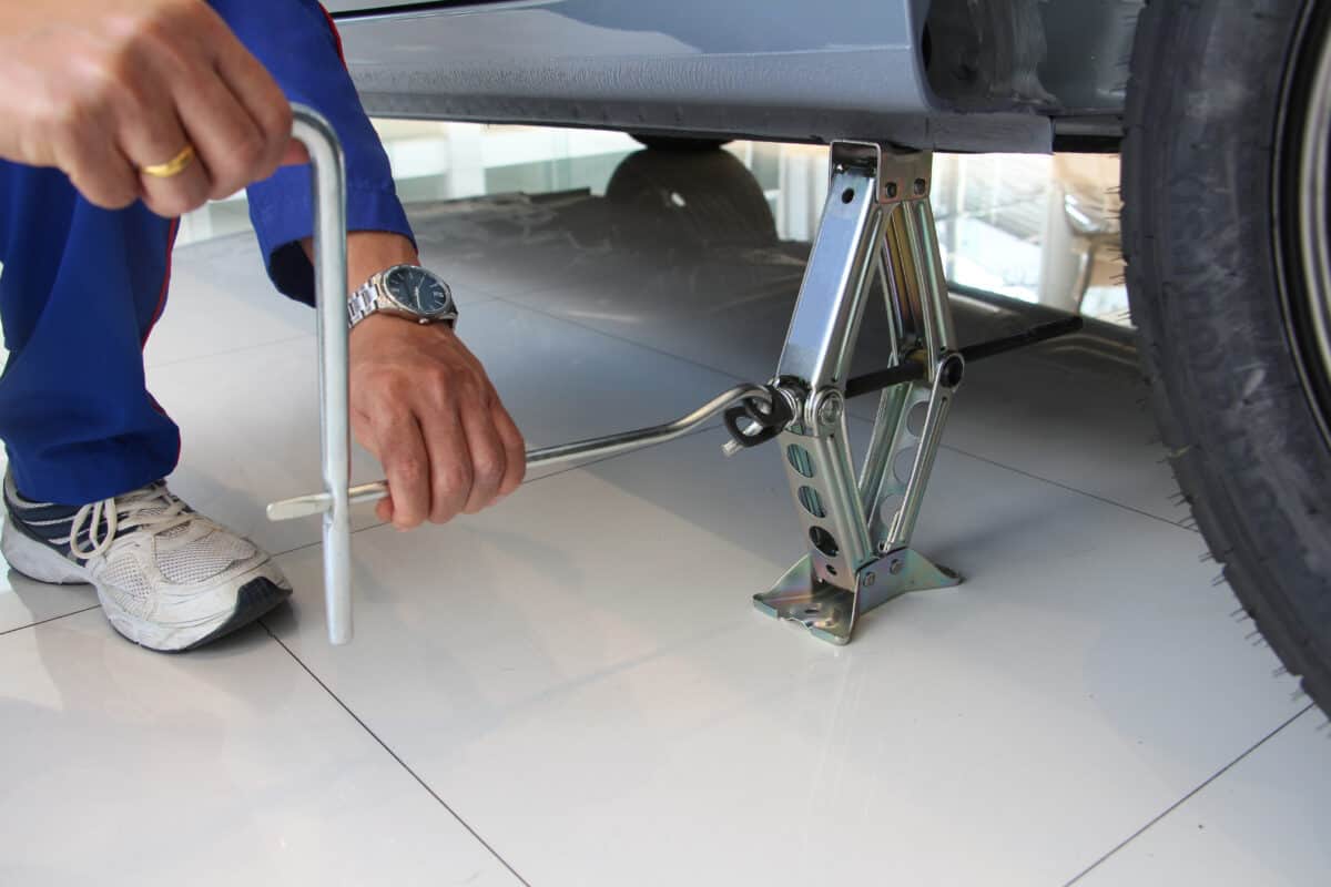 A mechanic using a silver scissor jack to hold up a car