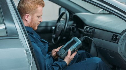 Mechanic sitting in car looking at an OBD2 scanner display