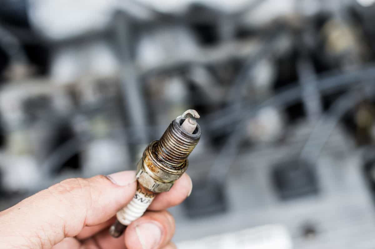 A mechanics holding up an old, oily spark plug