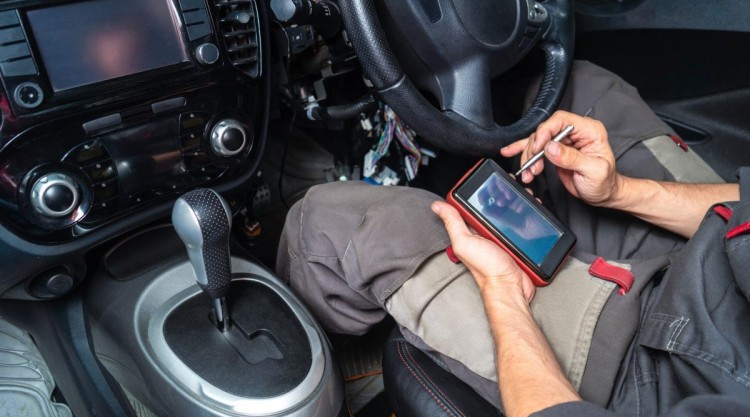Man sitting in car, readinfg from a smartphone the info sent by a Bluetooth obd II scanner