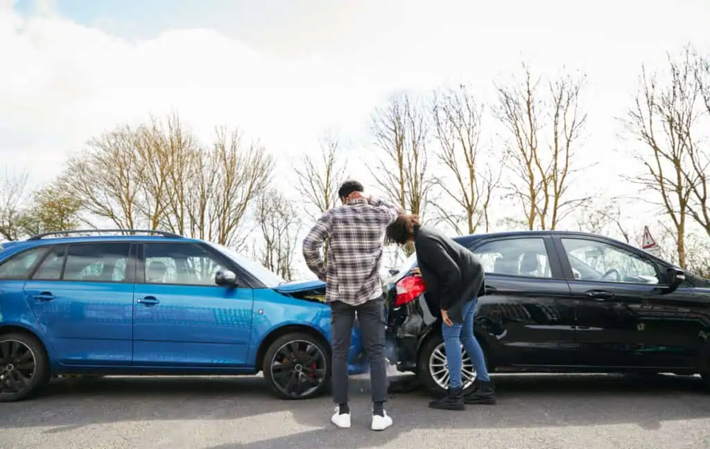 Two people looking at the aftermath of a blue and black car crashing into eachother