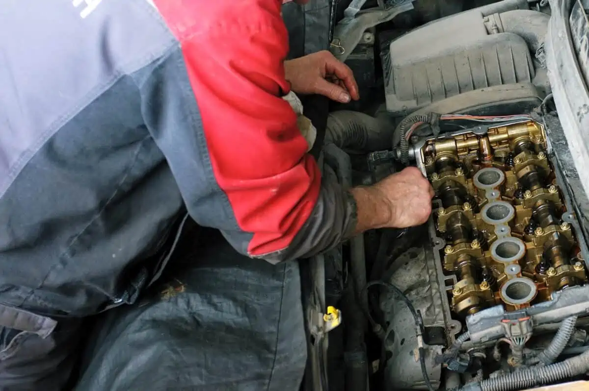 A mechanic with red sleeves inside an engine, with the valve cover removed