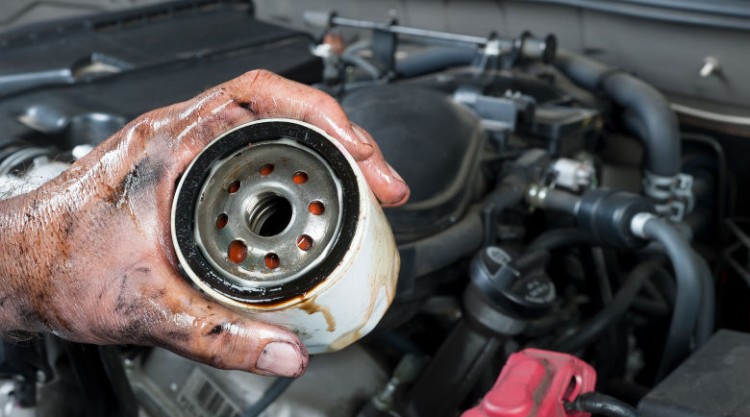 A mechanic holding an oil filter, with a car engine in the background