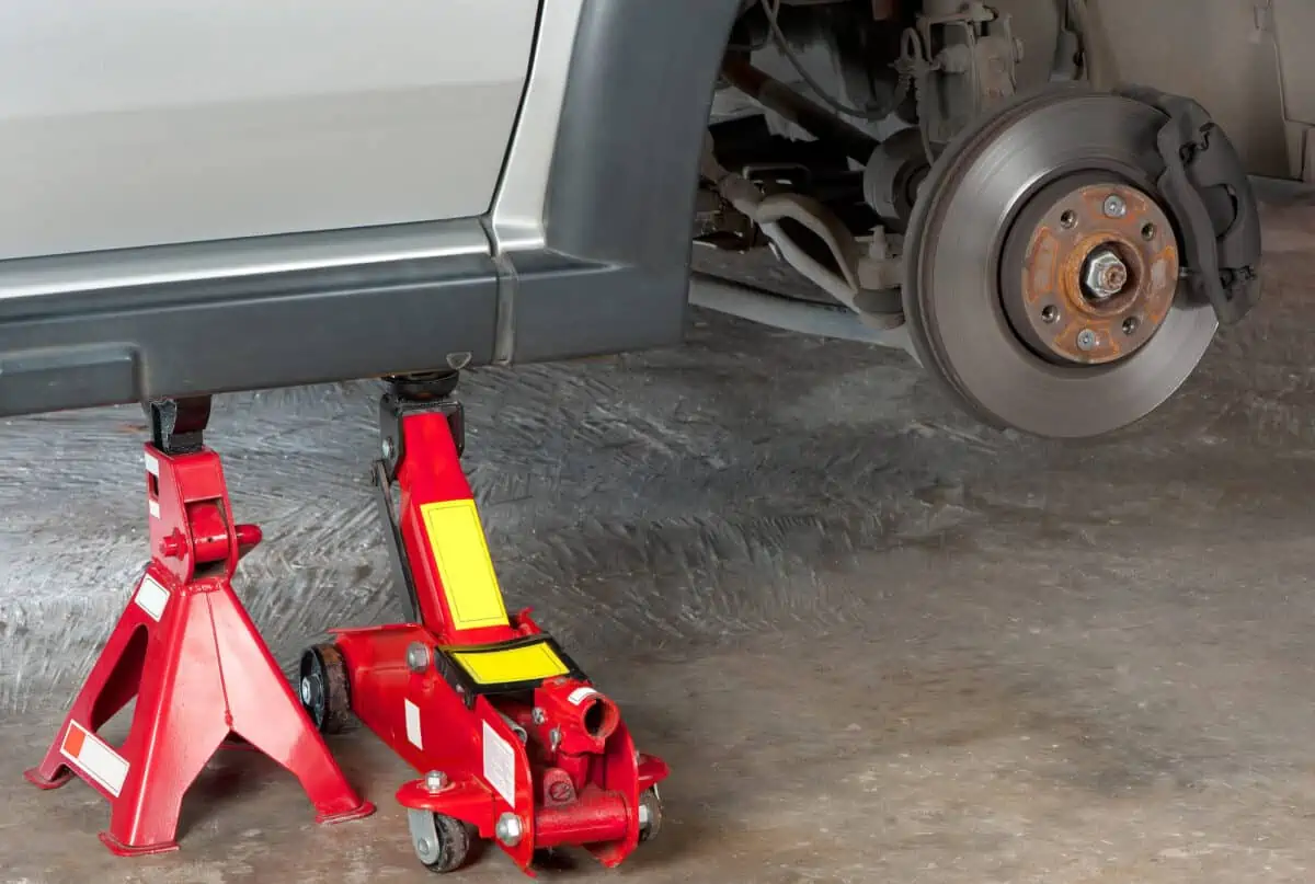 A car being held up by a red floor jack, and red jack stand