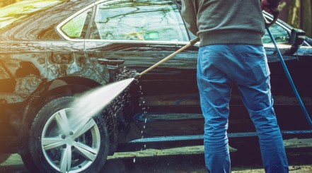 Man with pressure washer cleaning the rear wheel of his black car