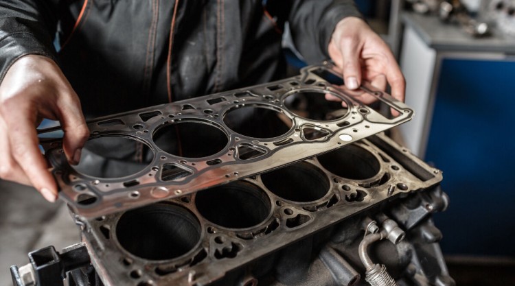 A mechanic holding a head gasket in his hand, standing over the engine