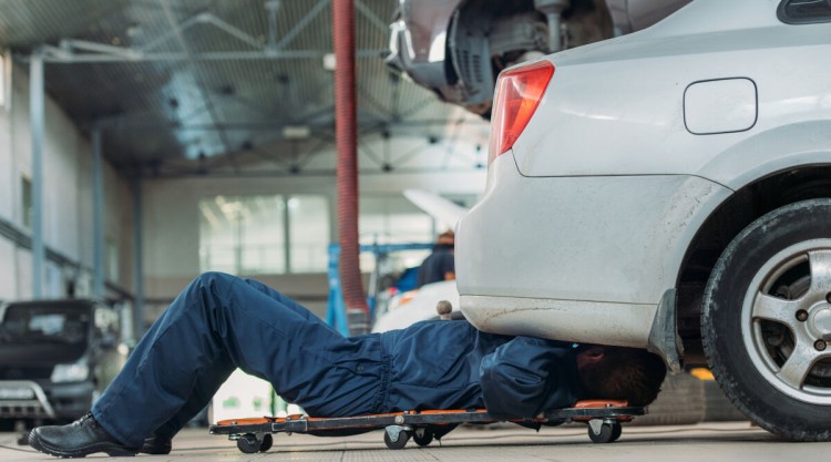 A mechanic sliding on a creeper under a silver car