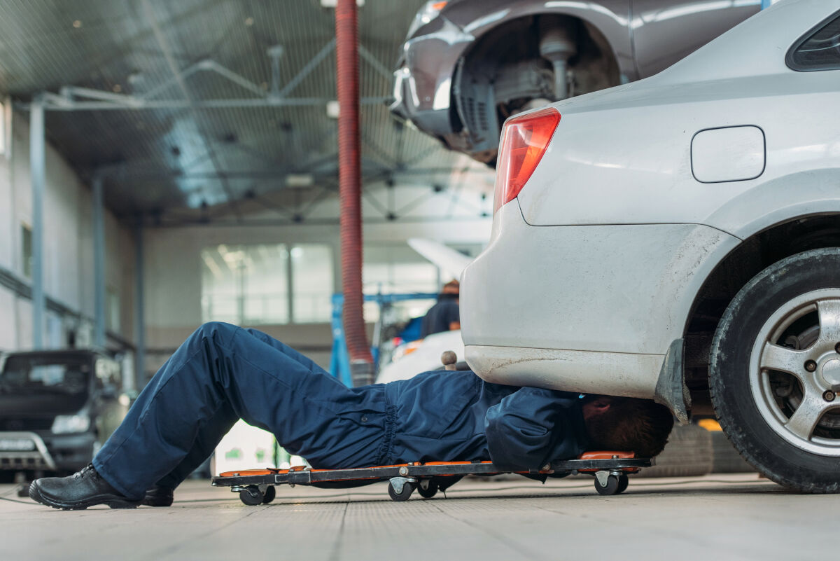 A mechanic sliding on a creeper under a silver car