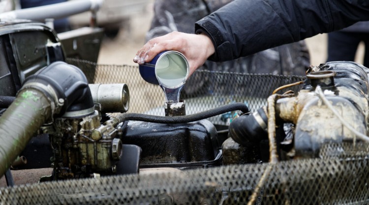 A mechanic pouring engine oil additive into an older looking engine