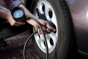 A mechanic using a tire pressure gauge outside on a front tire