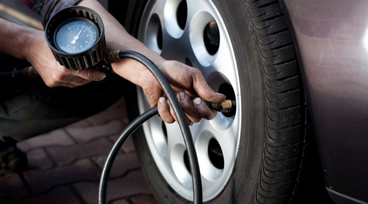 A mechanic using a tire pressure gauge outside on a front tire