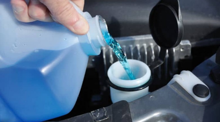 Some blue windshield washer fluid being poured into a car