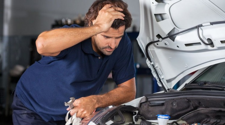 Mechanic leaning on the edge of a car hood, trying to figure out what