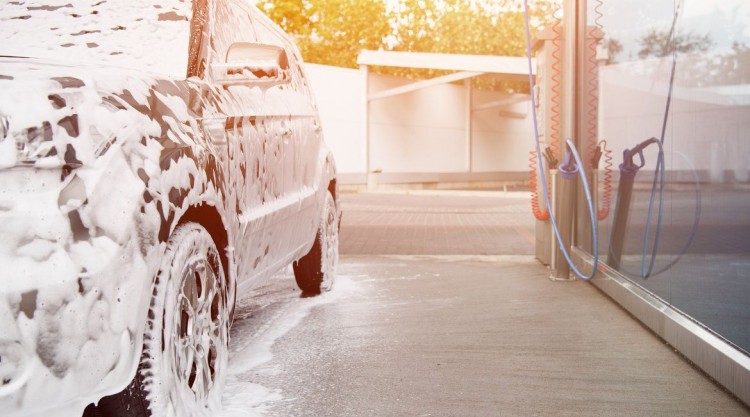 A car with foam all over its exterior, and a foam cannon next to it