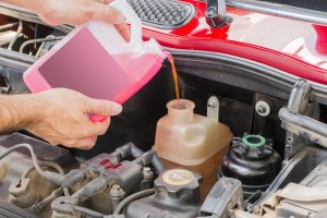 Man pouring pink antifreeze from bottle into the car