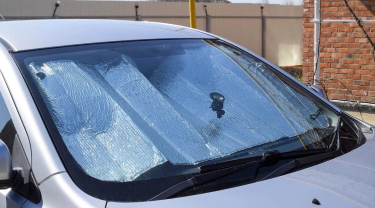 Parked silver car with a sun shade placed inside that covers its windshield