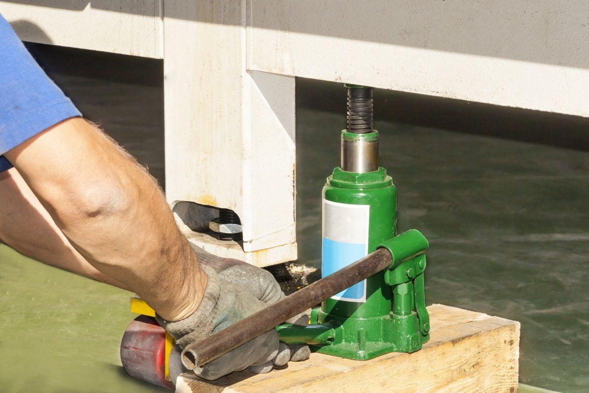 A mans gloved hand operating a green bottle jack