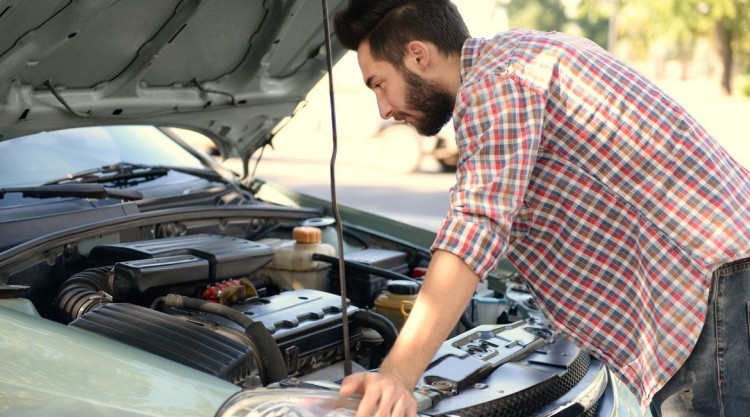 Young man inspecting the hood of his vehicle on the side of the road because of overheating problems