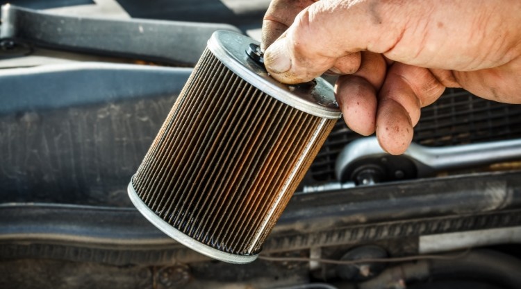 Mechanic holding a dirty fuel filter that needs replacement