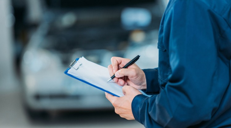 Mechanic holding a notebook and pen to jot down notes about a car