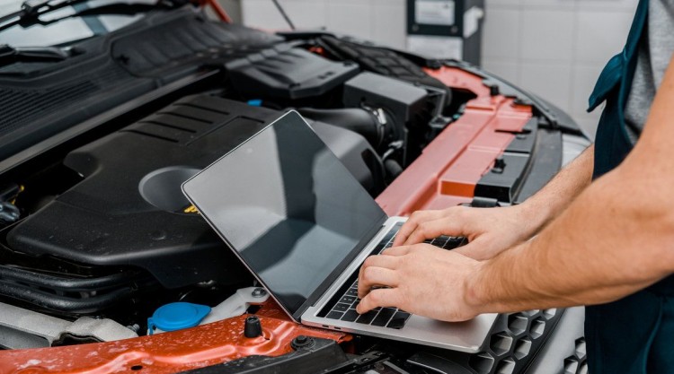 Car in a garage service shop with mechanic working on the laptop for data entry regarding maintenance tasks