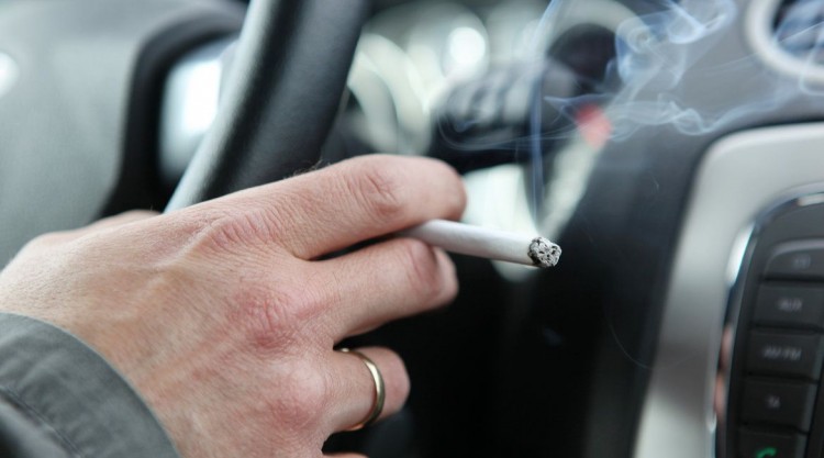 Man driving car with right hand on the steering wheel while holding a burning cigarette