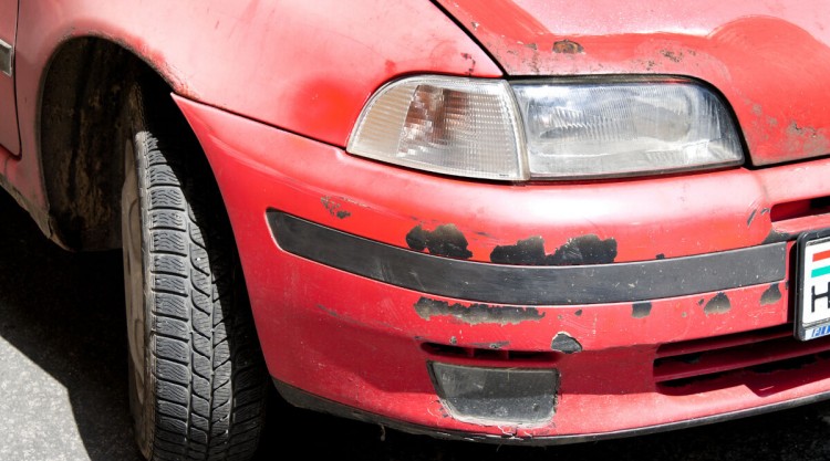 Red car with damaged exterior paint because of rust