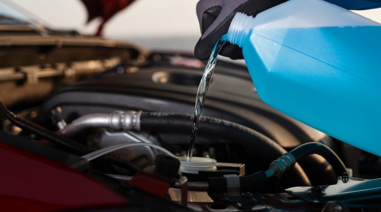 Car owner wearing protective gloves while pouring antifreeze into his car