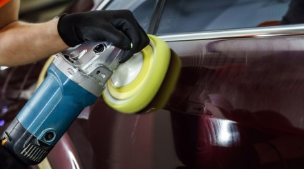 A motorized buffer being used on a dark car door