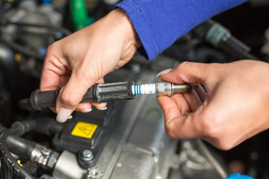 Man in blue overalls holding a spark plug above an engine