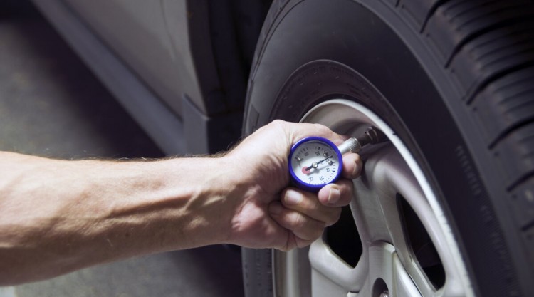 A mans hand pressing a tire pressure gauge onto a car tire