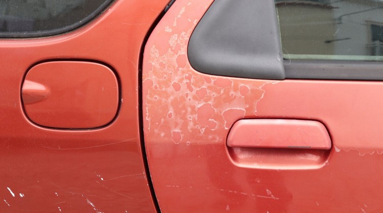 Close up on red colored car with faded and damaged paint on door that needs restoring