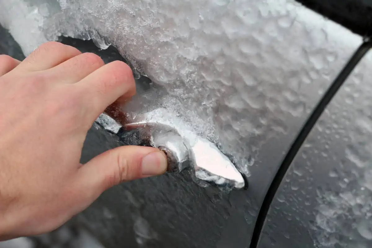A mans hand trying to open a frozen car door