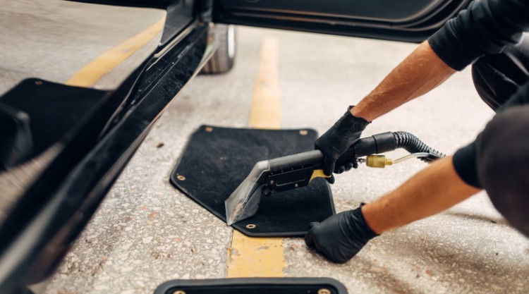 Man cleaning car mats with a steam cleaner or vacuum