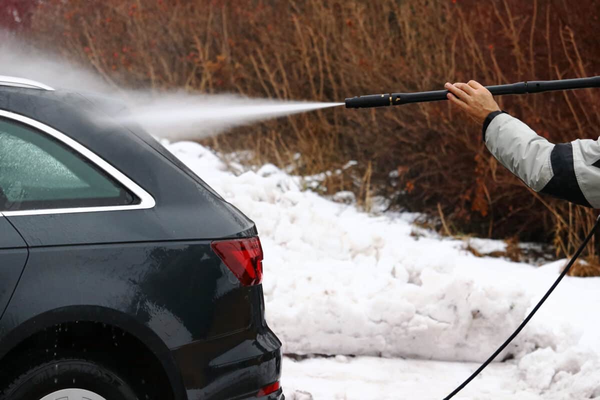 Jet washing the back of a black car, with snow on the ground in the background