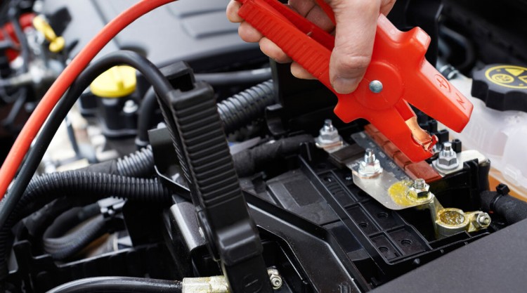 Person working on his car battery with a jumper cable to jump start his vehicle