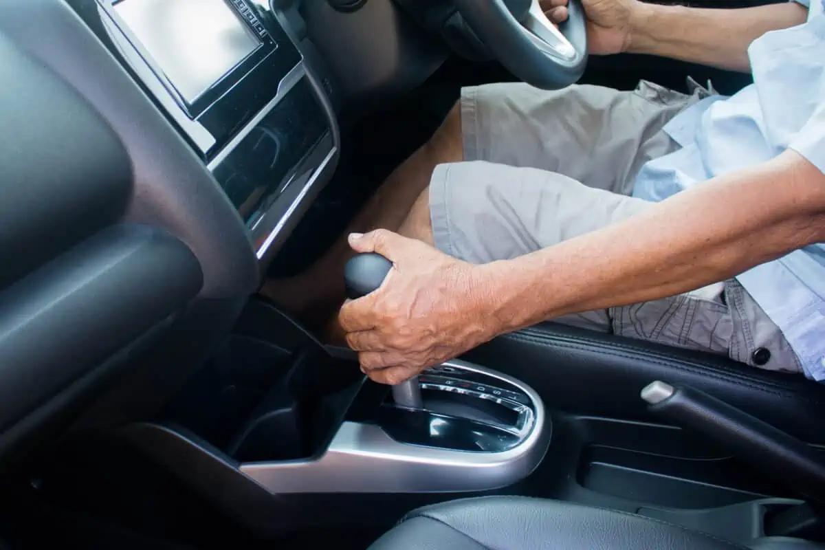 A man driving an automatic transmission car, with one hand on steering wheel and the other on the gear stick