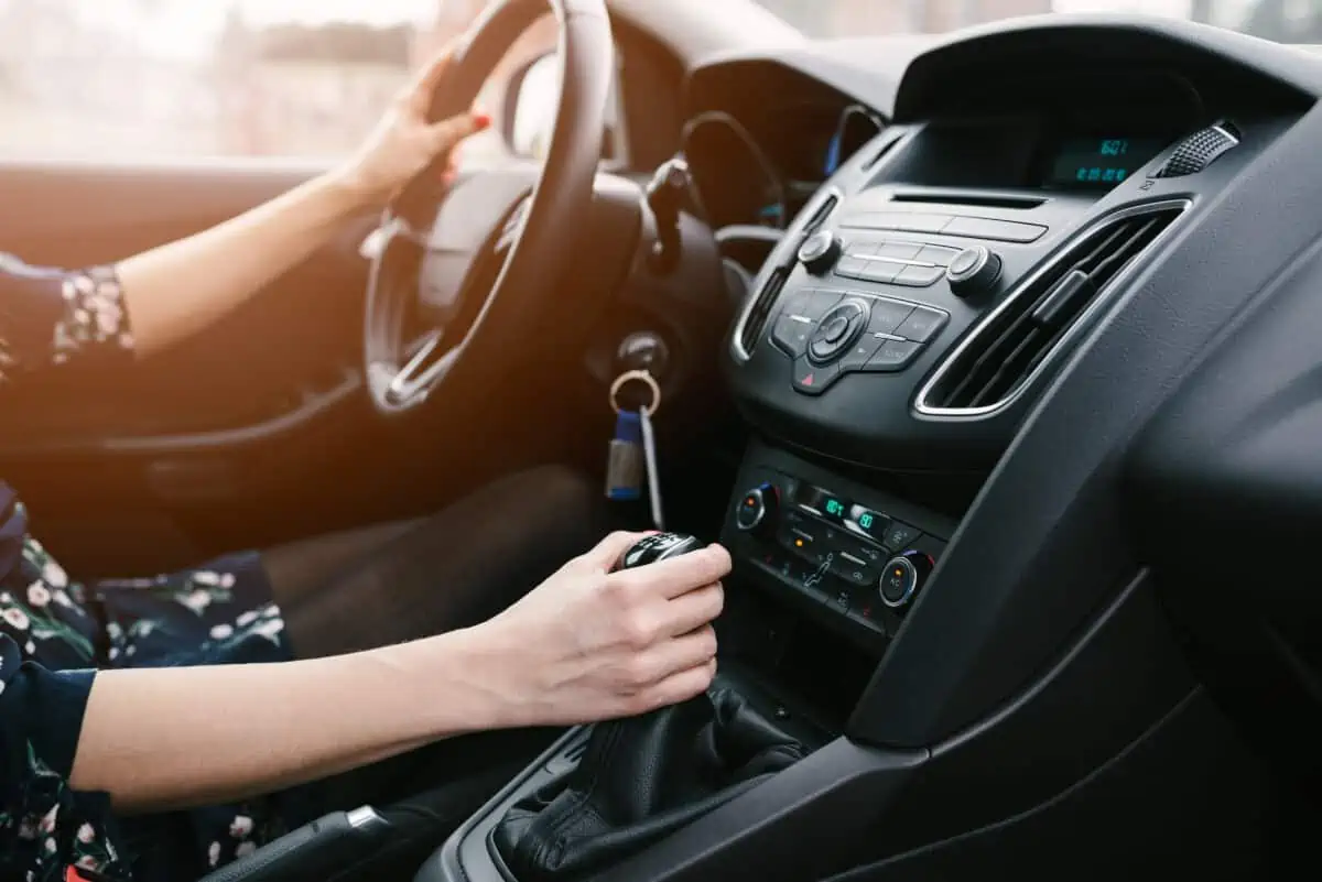 A woman driving a manual transmission car, with one hand on steering wheel and the other on the gear stick