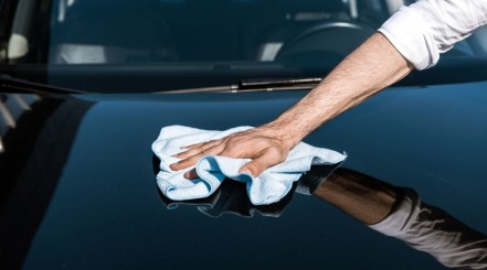 Man wiping his car's surface with a towel after finishing removing swirl marks