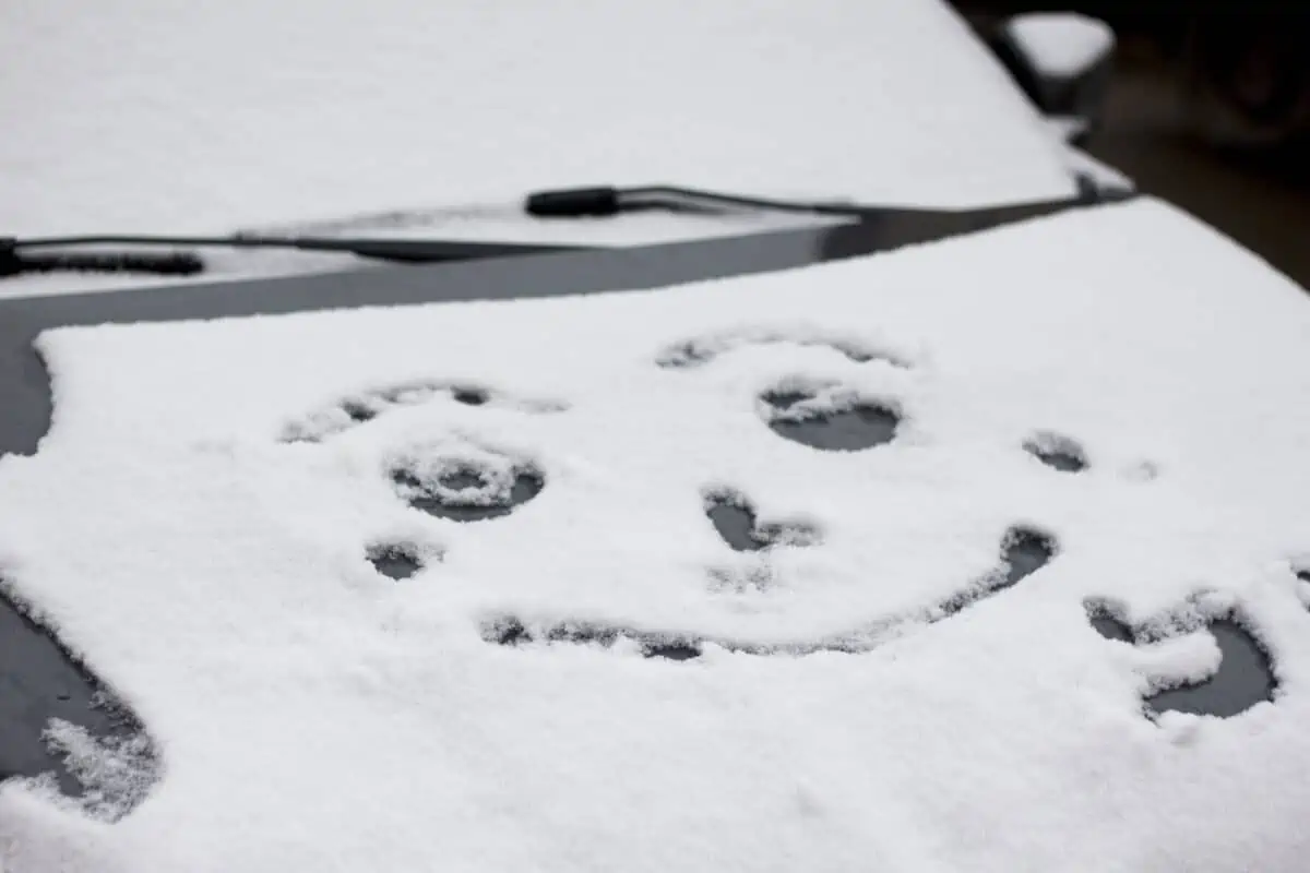 A smiley face drawn in the snow on a car bonnet