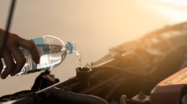 A mans hand pouring water into the coolant reservoir of a car engine