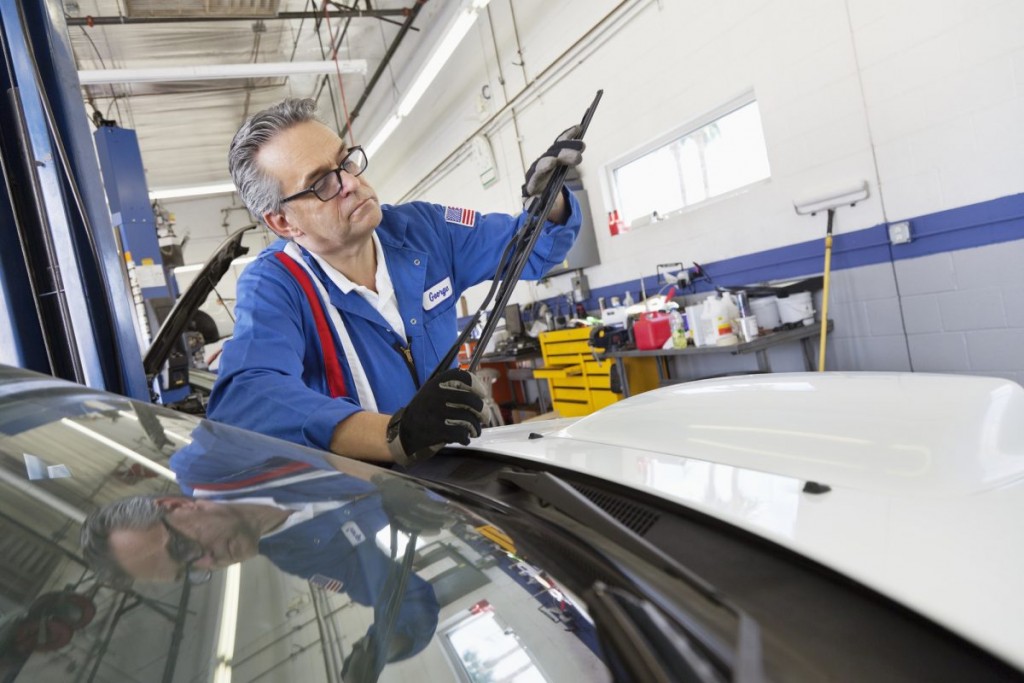 Car mechanic in blue overalls inspecting windshield wipers