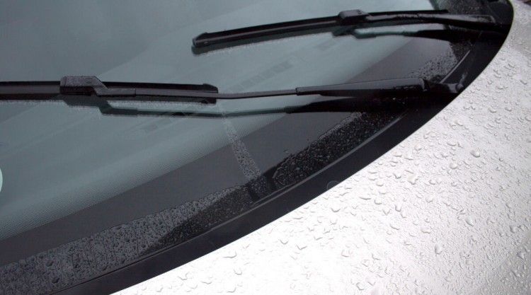 Wet silver car from rain, and windshield wipers working to clear the windshield